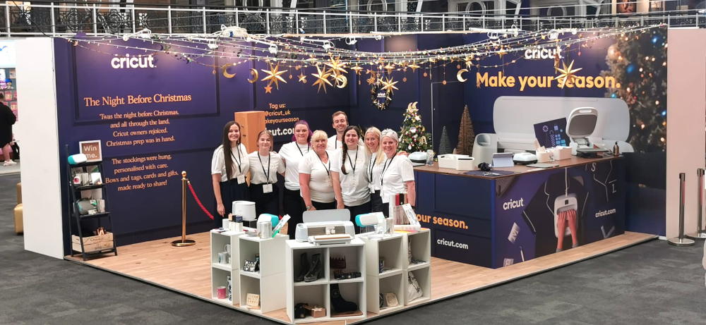 A group of people in front of a Cricut stall posing for a photo at an industry event.