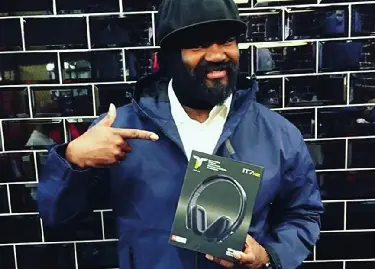 A man standing in front of a wall pointing towards an IT7 headphone box and smiling.